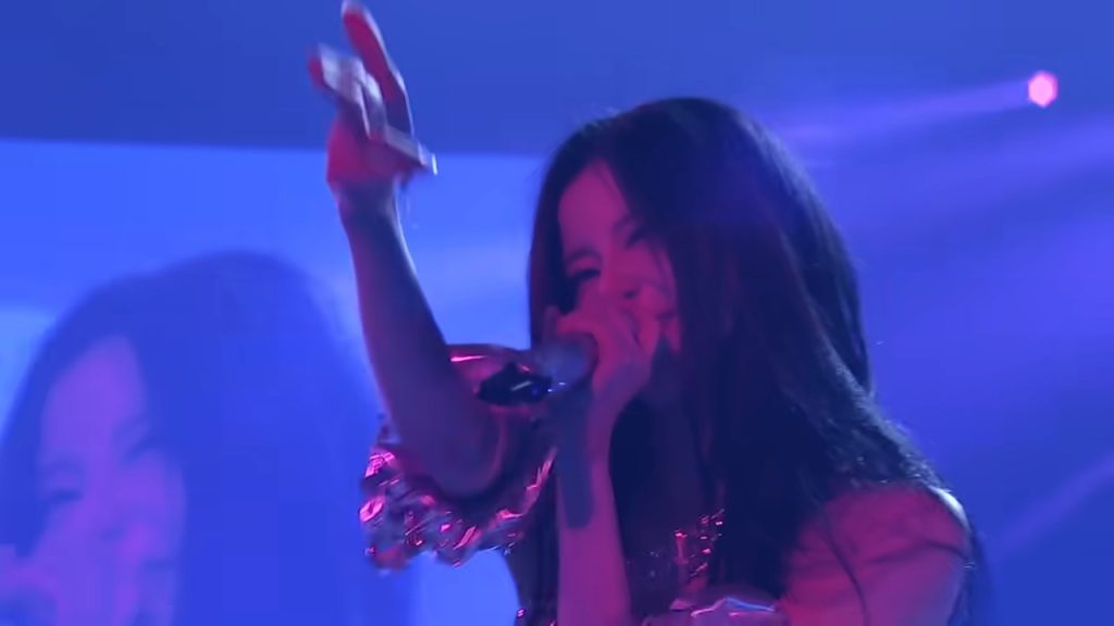 BABYMONSTER member performing live with a handheld microphone on the Hello Monsters world tour stage