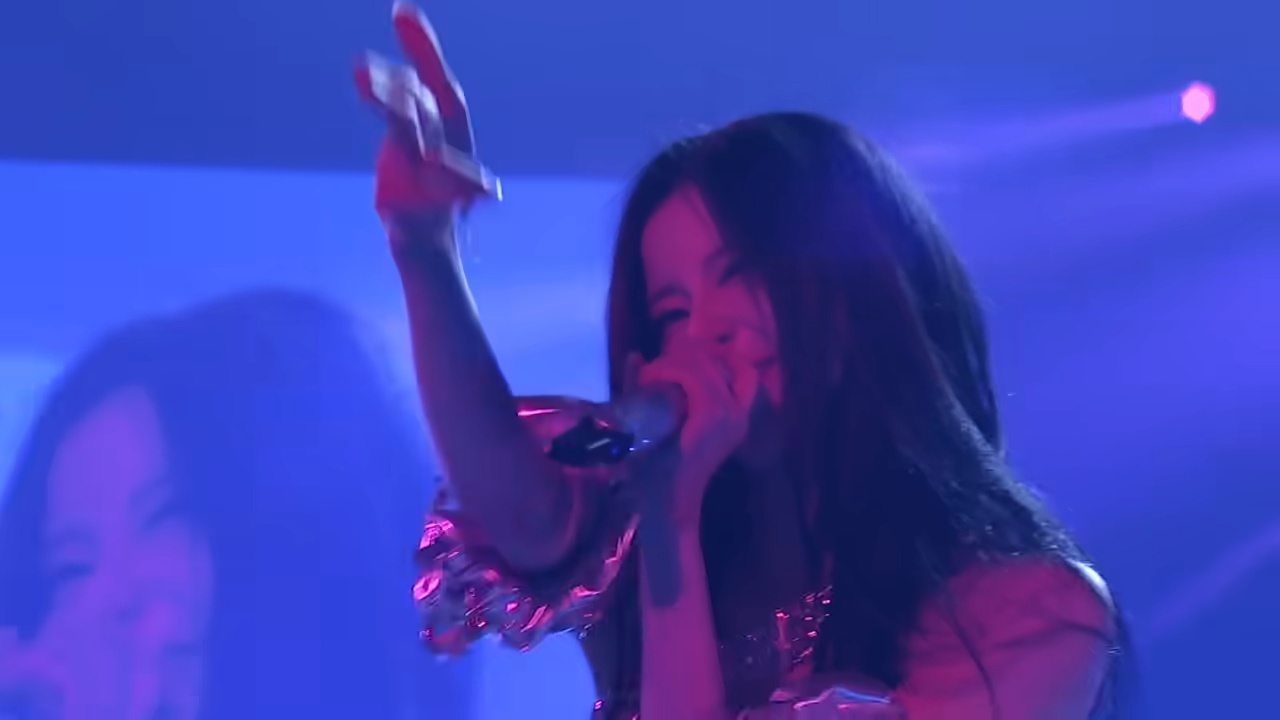 BABYMONSTER member performing live with a handheld microphone on the Hello Monsters world tour stage