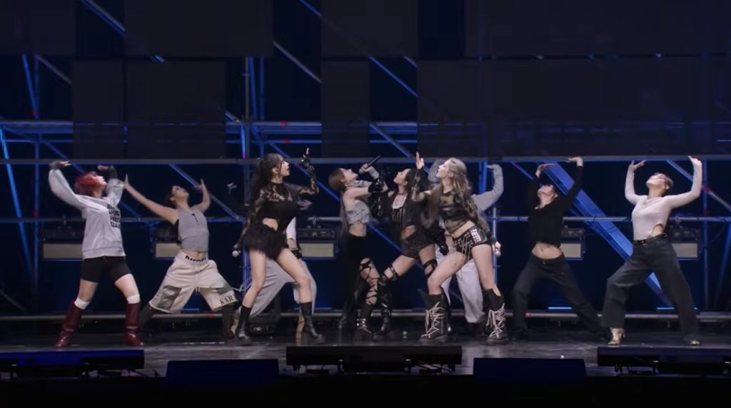 KISS OF LIFE performing 'Who Is She' live on stage, holding microphones while dancing with backup dancers