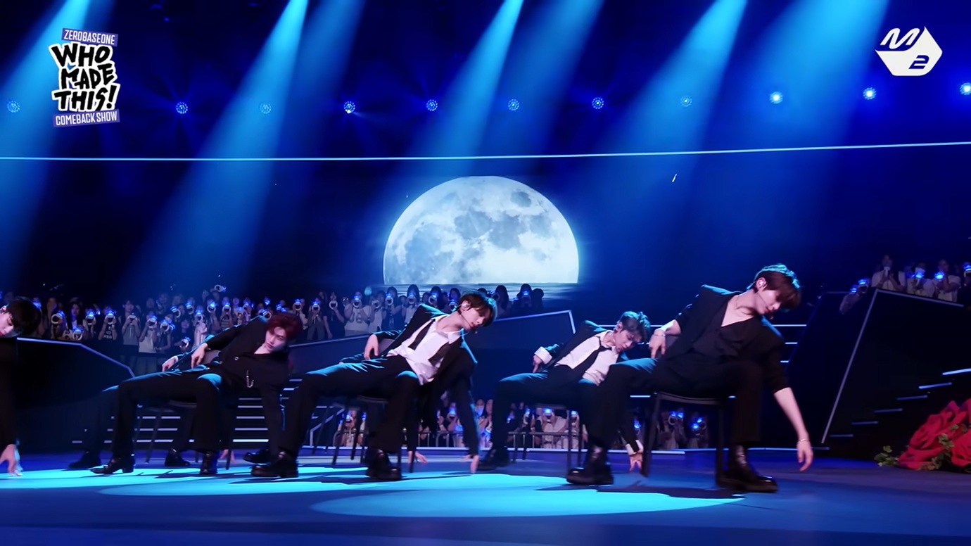 The nine members of ZEROBASEONE performing the chair choreography for 'Lovesick Game' on a moonlit blue stage