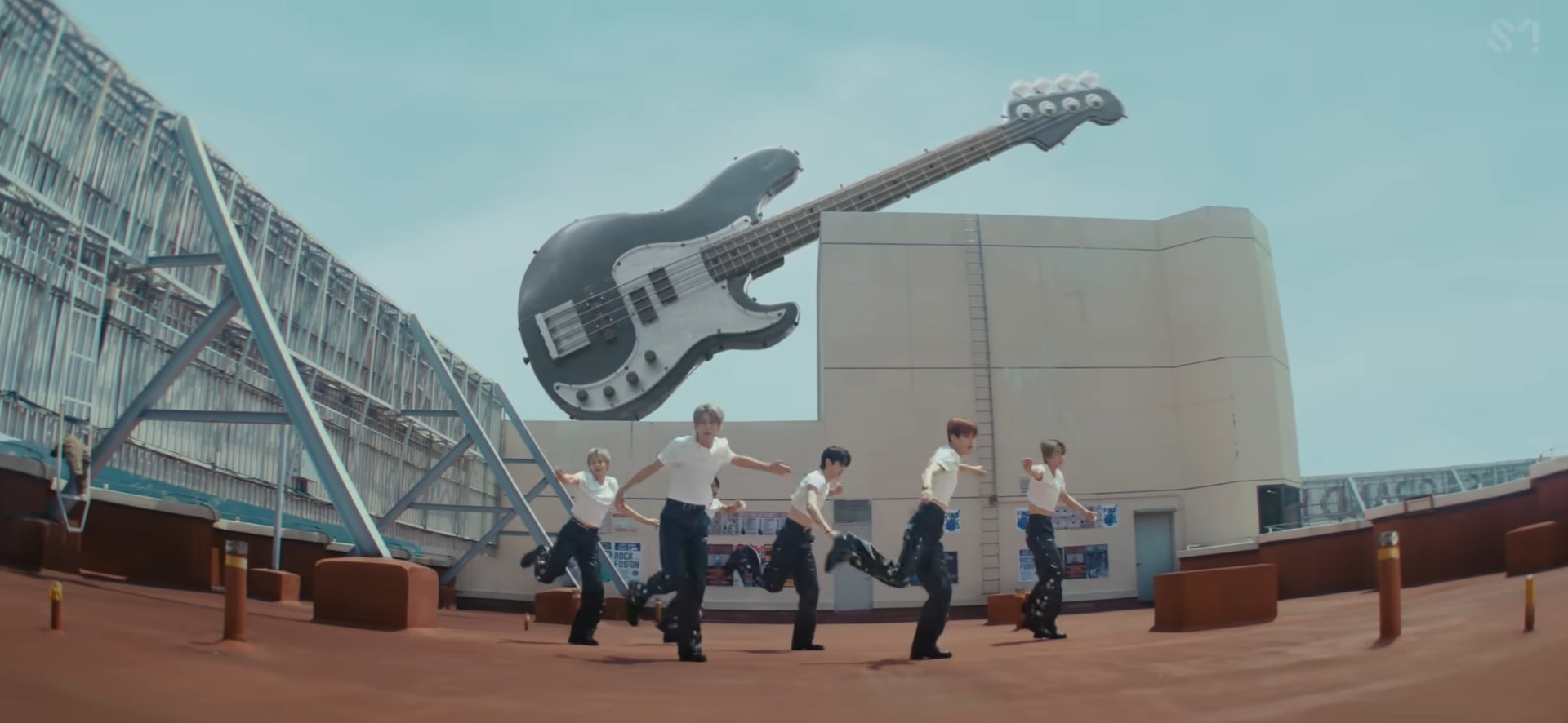 RIIZE performing a group dance in front of a giant bass guitar sculpture in the Boom Boom Bass music video