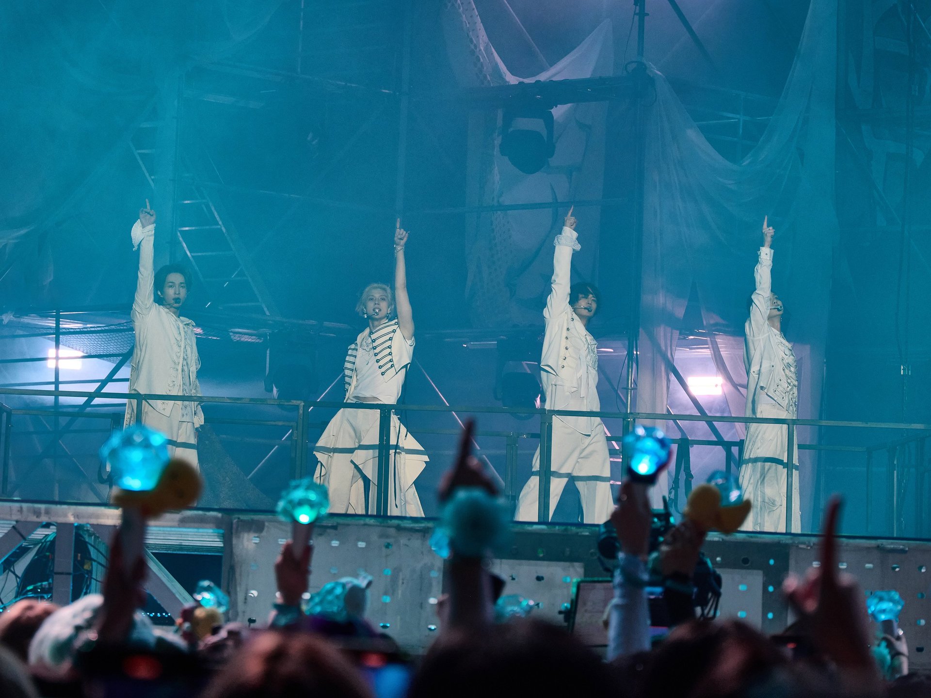 Membrii SHINee ridică o mână cu același gest și în același moment pe scena unui concert