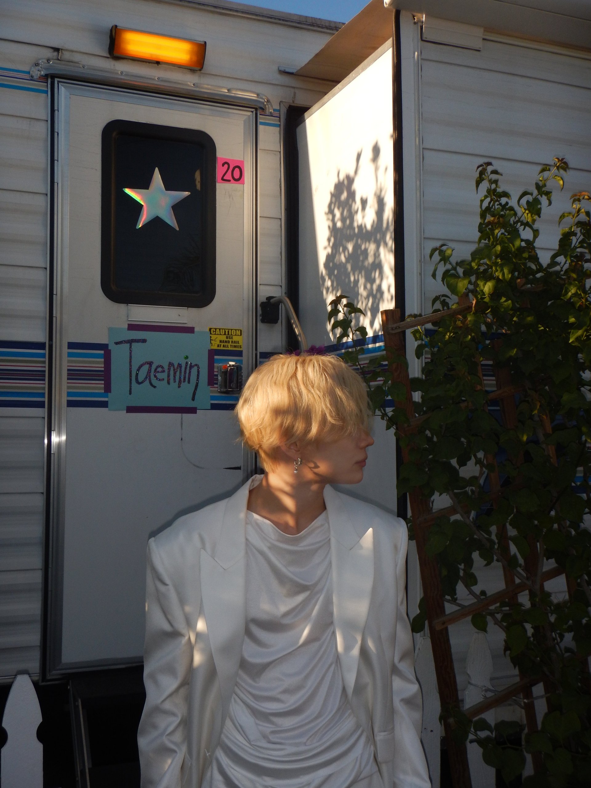 TAEMIN standing outside his Coachella dressing room, with a handwritten sign bearing his name taped to the door