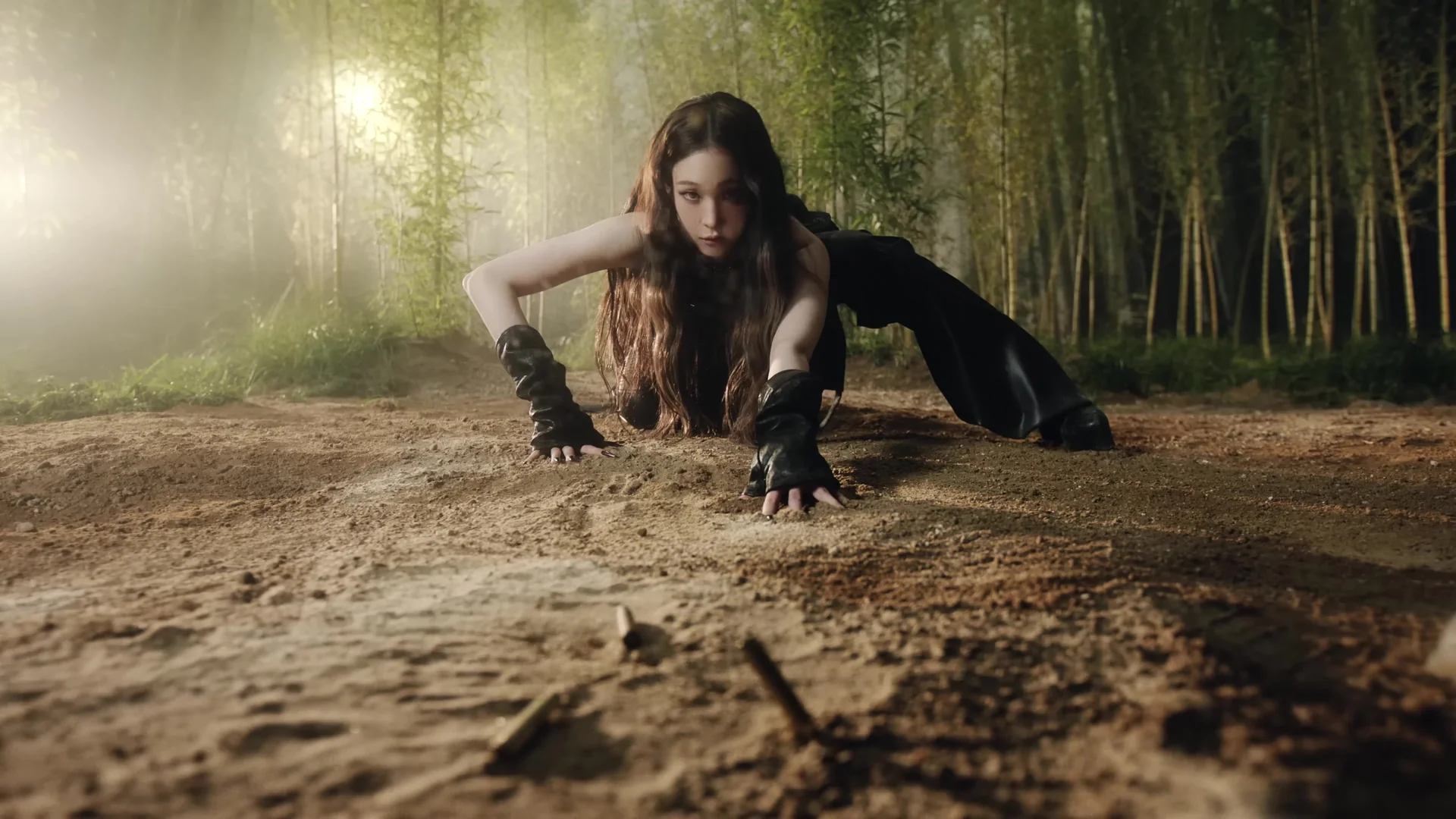 ALLDAY PROJECT's Annie crouching low on the dirt in a bamboo forest scene from the I DON'T BARGAIN music video, looking straight ahead