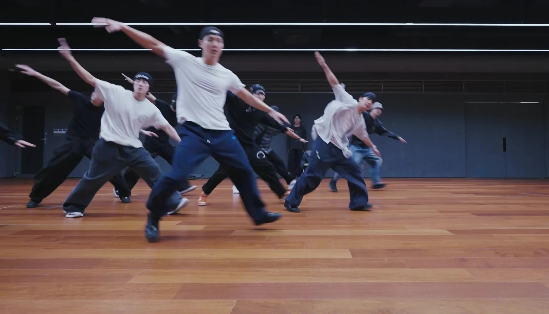 MONSTA X und Tänzer strecken in einer Probenformation gleichzeitig die Arme aus