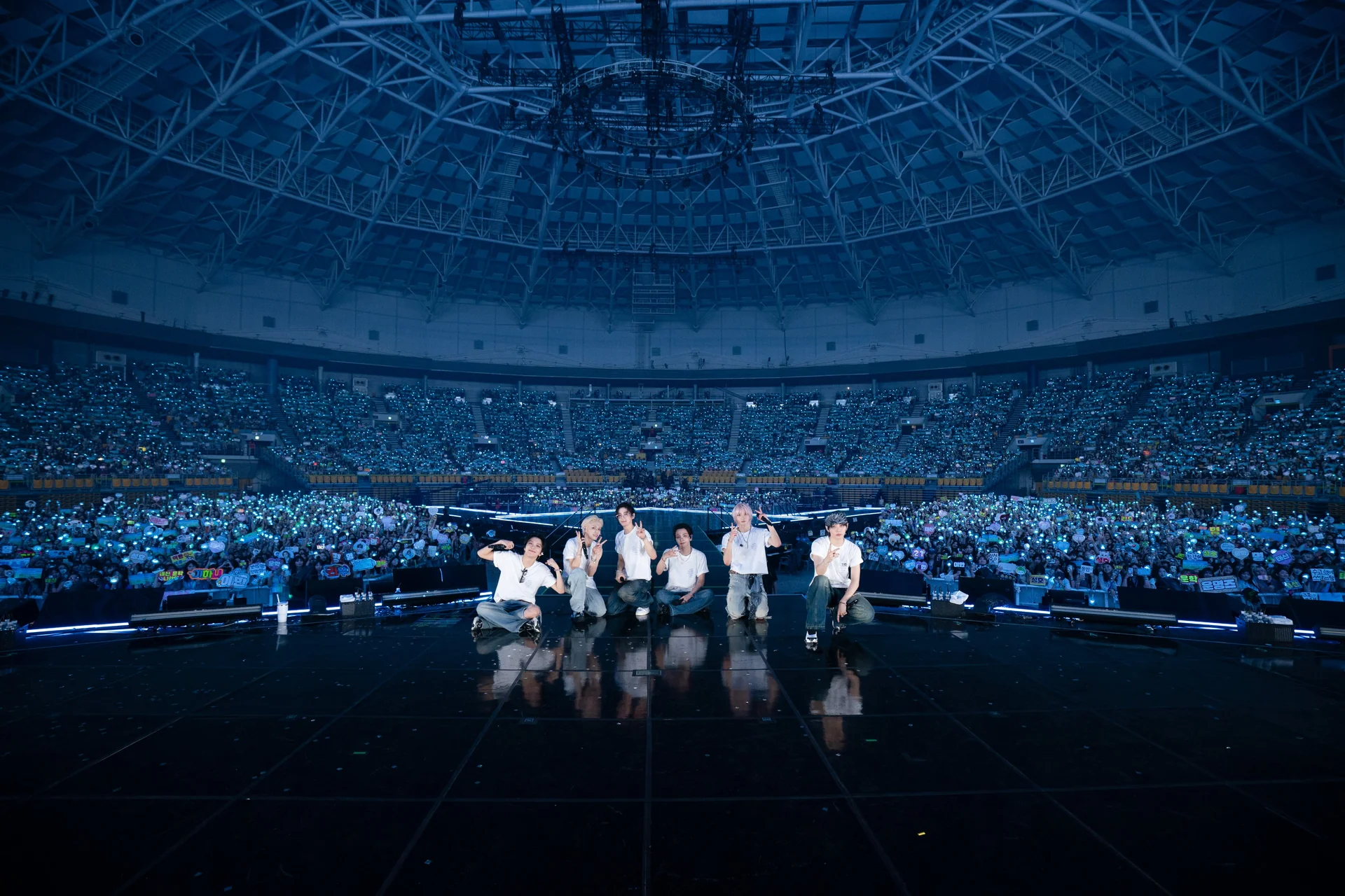 The six members of BOYNEXTDOOR standing at the front of the stage with a packed KSPO Dome lit in blue behind them